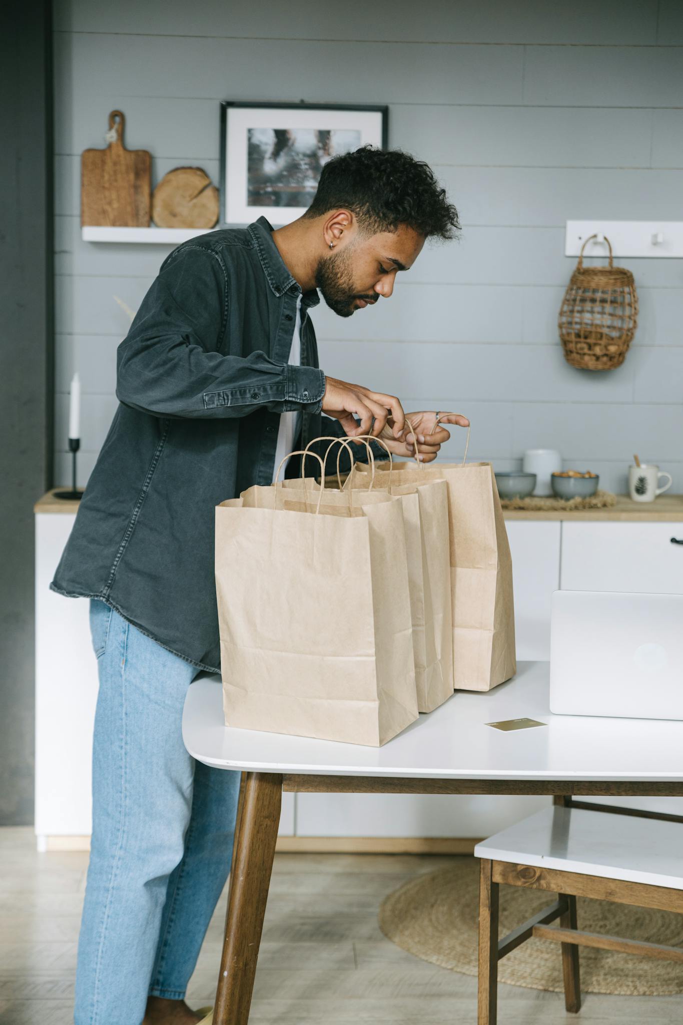 Young man organizing paper shopping bags indoors in a modern kitchen setting.